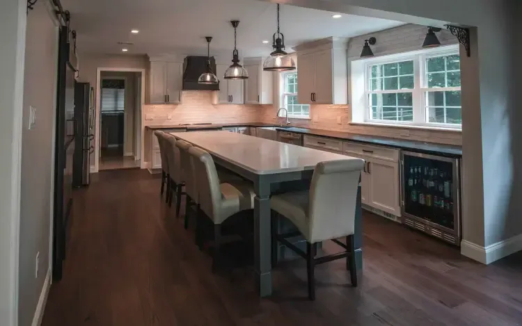 Modern kitchen with large island, pendant lights, barstools, and a wine cooler by a window