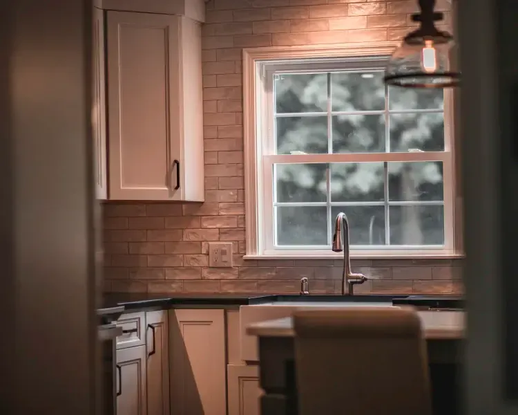 Cozy kitchen with wood cabinets, subway tile, sink by a window, and a hanging light fixture.