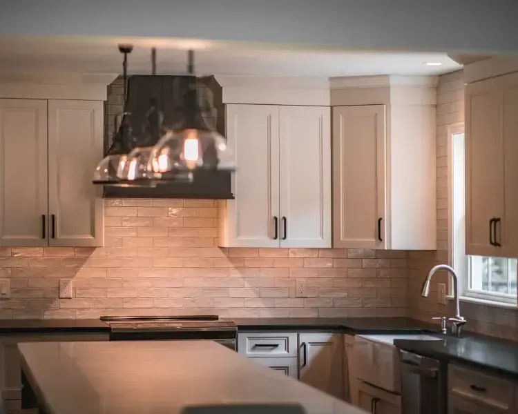 Modern kitchen with white cabinets, dark countertop, brick backsplash, and a large stainless range hood
