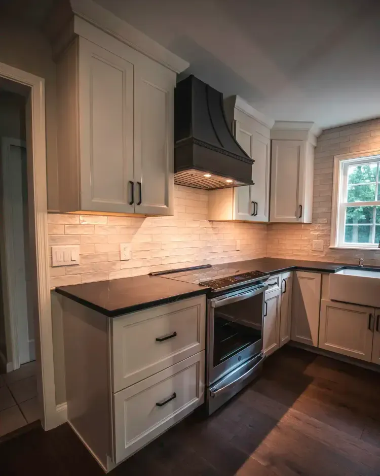 Modern kitchen with gray cabinets, black range hood, white tile backsplash, and dark wood floors