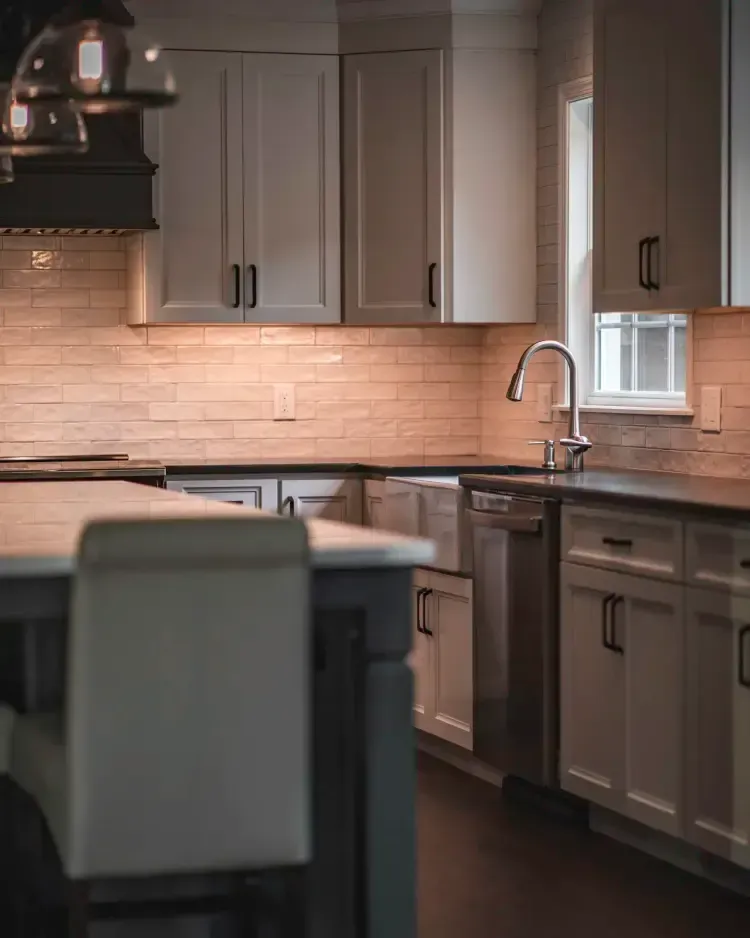 Modern kitchen with gray cabinets, stainless sink, and dark countertops, lit by warm natural light