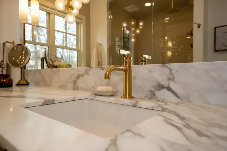 Marble bathroom vanity with gold faucet, large mirror, and warm pendant lights
