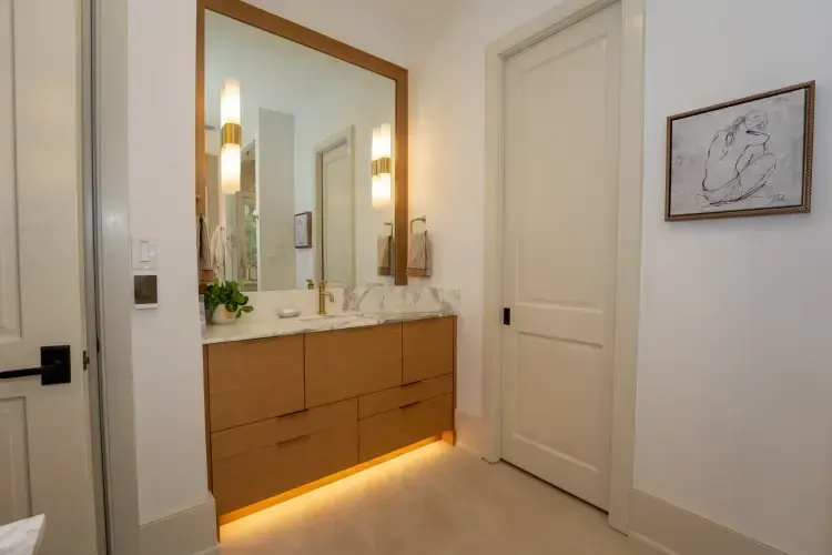 Modern bathroom vanity with large mirror, warm sconces, and under-cabinet lighting in a white room
