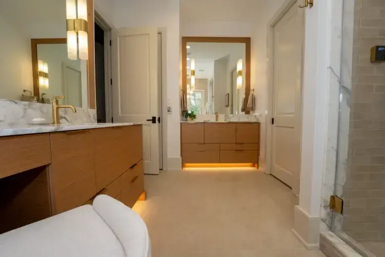Bright modern bathroom with double vanity, mirrors, white tile, and warm under-cabinet lighting.
