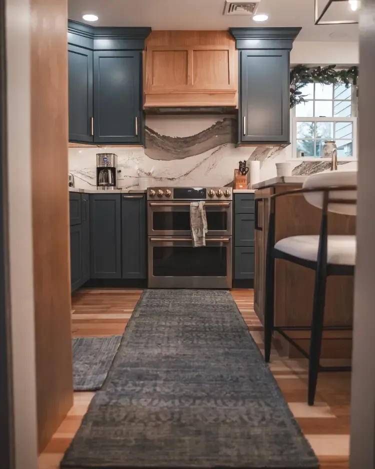 Modern kitchen with blue cabinets, wood accents, stainless stove, and a runner rug.
