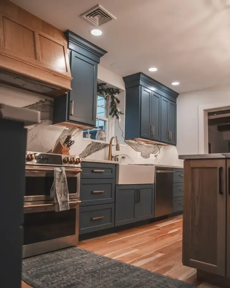 Modern kitchen with blue cabinets, stainless stove, white sink, hardwood floors, and ceiling lights.