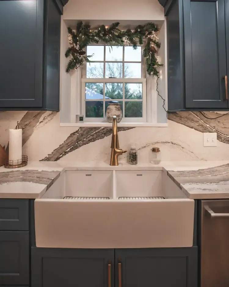 Kitchen sink beneath a window with garland, white countertops, and dark cabinets