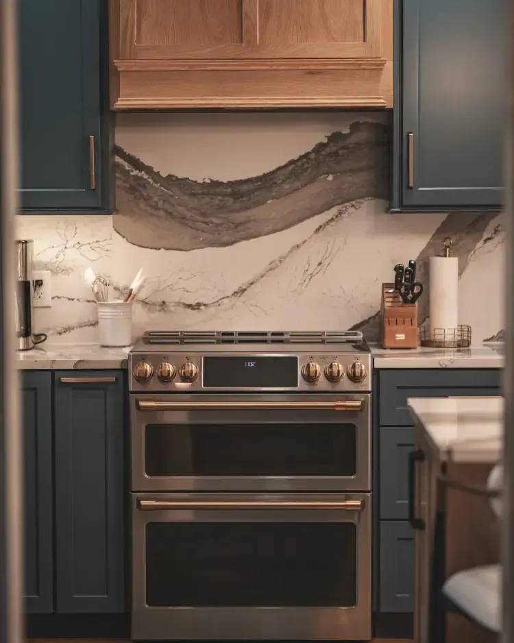 Modern kitchen with navy cabinets, marble backsplash, and stainless steel oven.