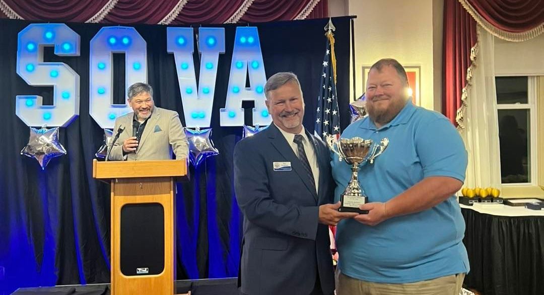 Two men holding a trophy in front of a sign that says SOVA