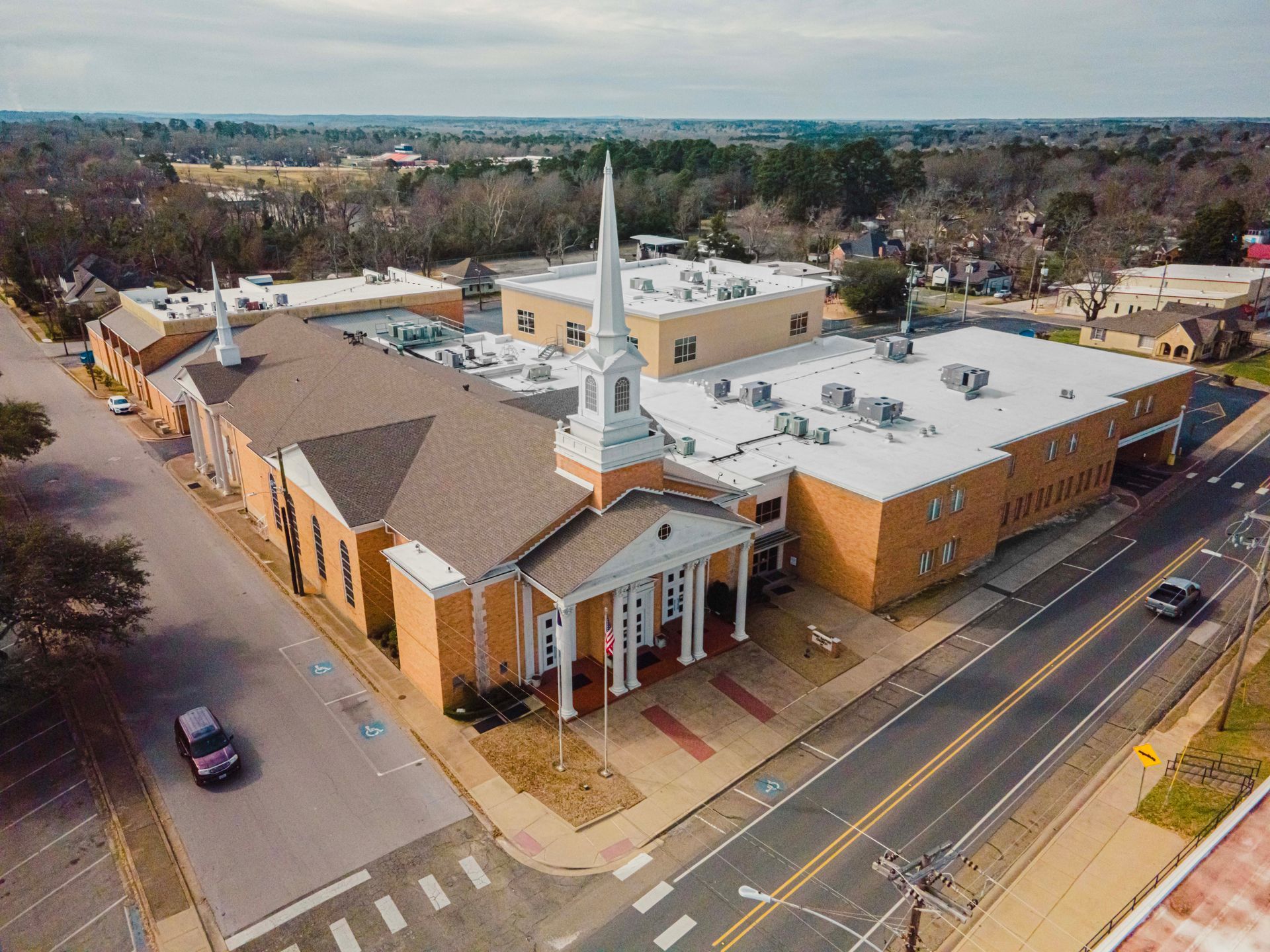An aerial view of a church in a small town with a car parked in front of it.