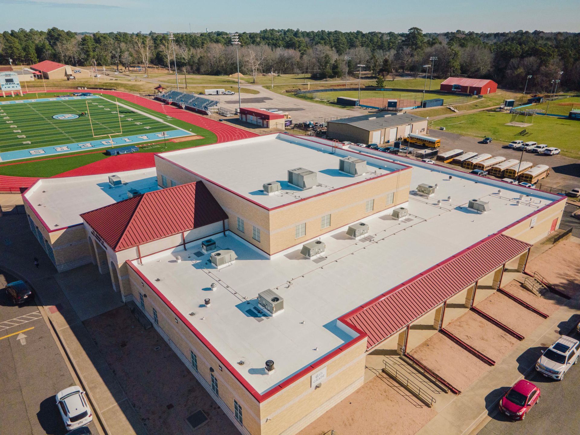 An aerial view of a large building with a red roof and a football field in the background.