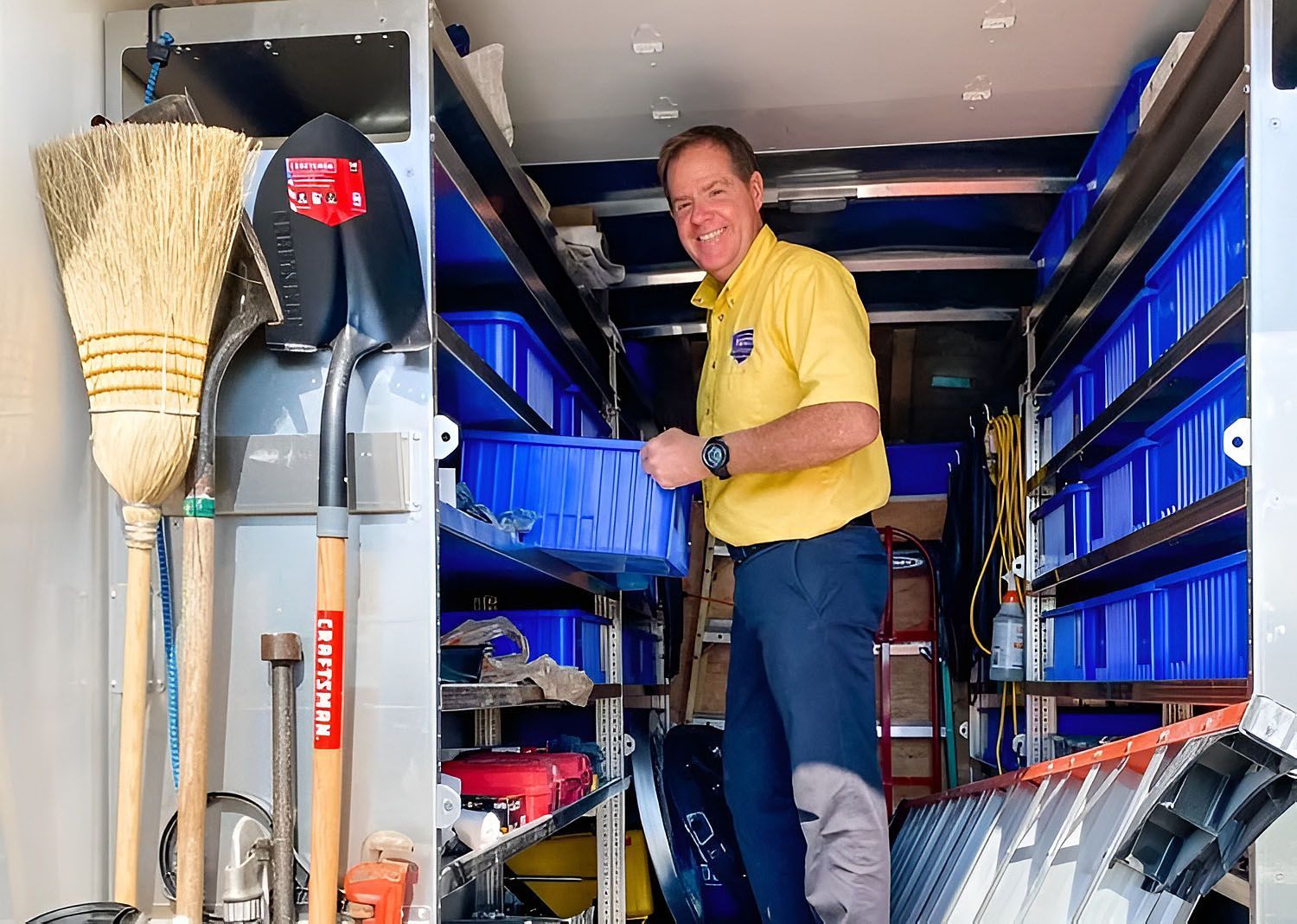 Man in yellow shirt standing in a utility truck, surrounded by tools and equipment.