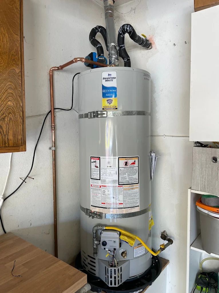 Large gray water heater with exposed pipes and venting in a utility room