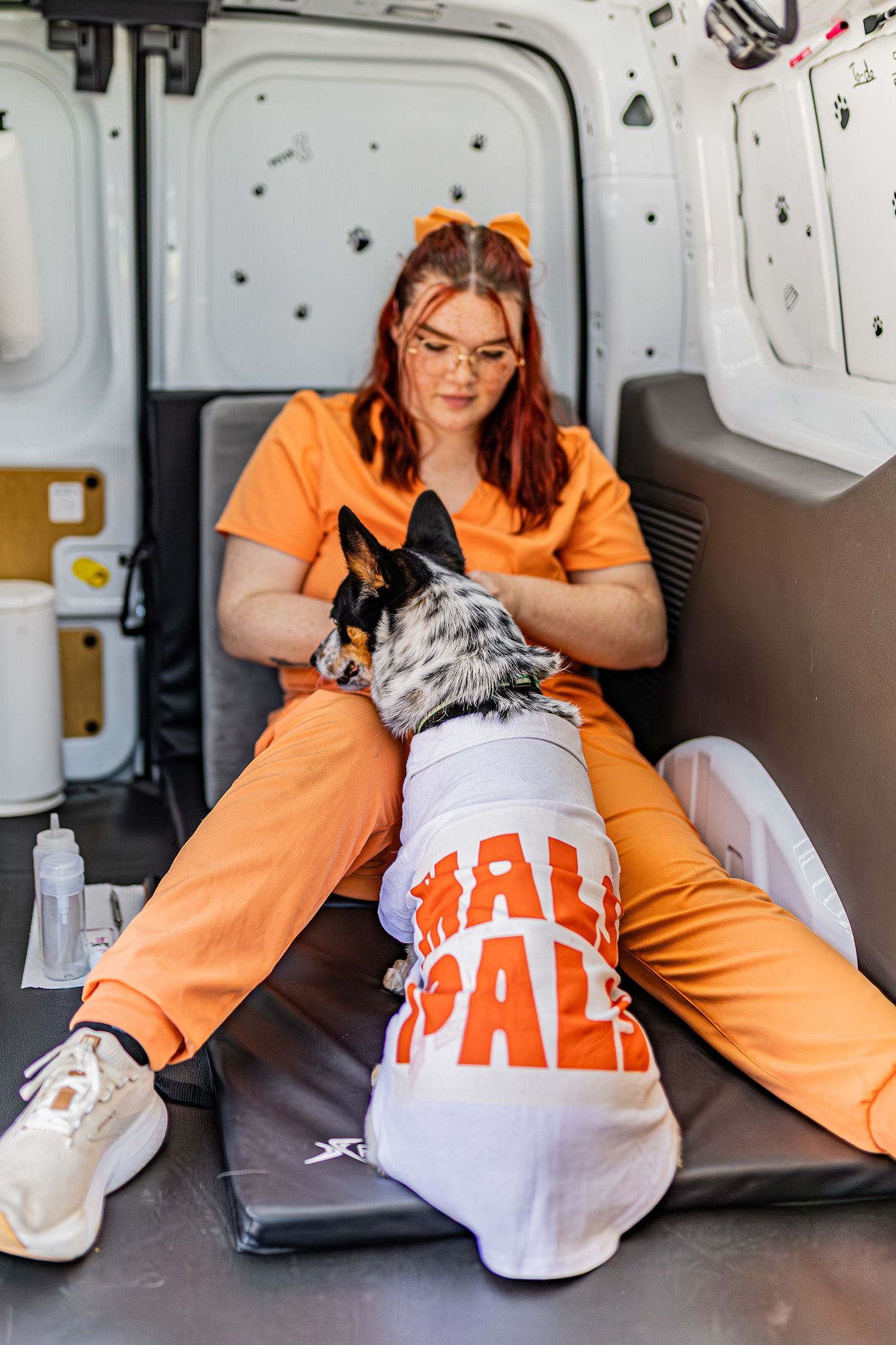 Woman in orange scrubs pets a dog wearing a 