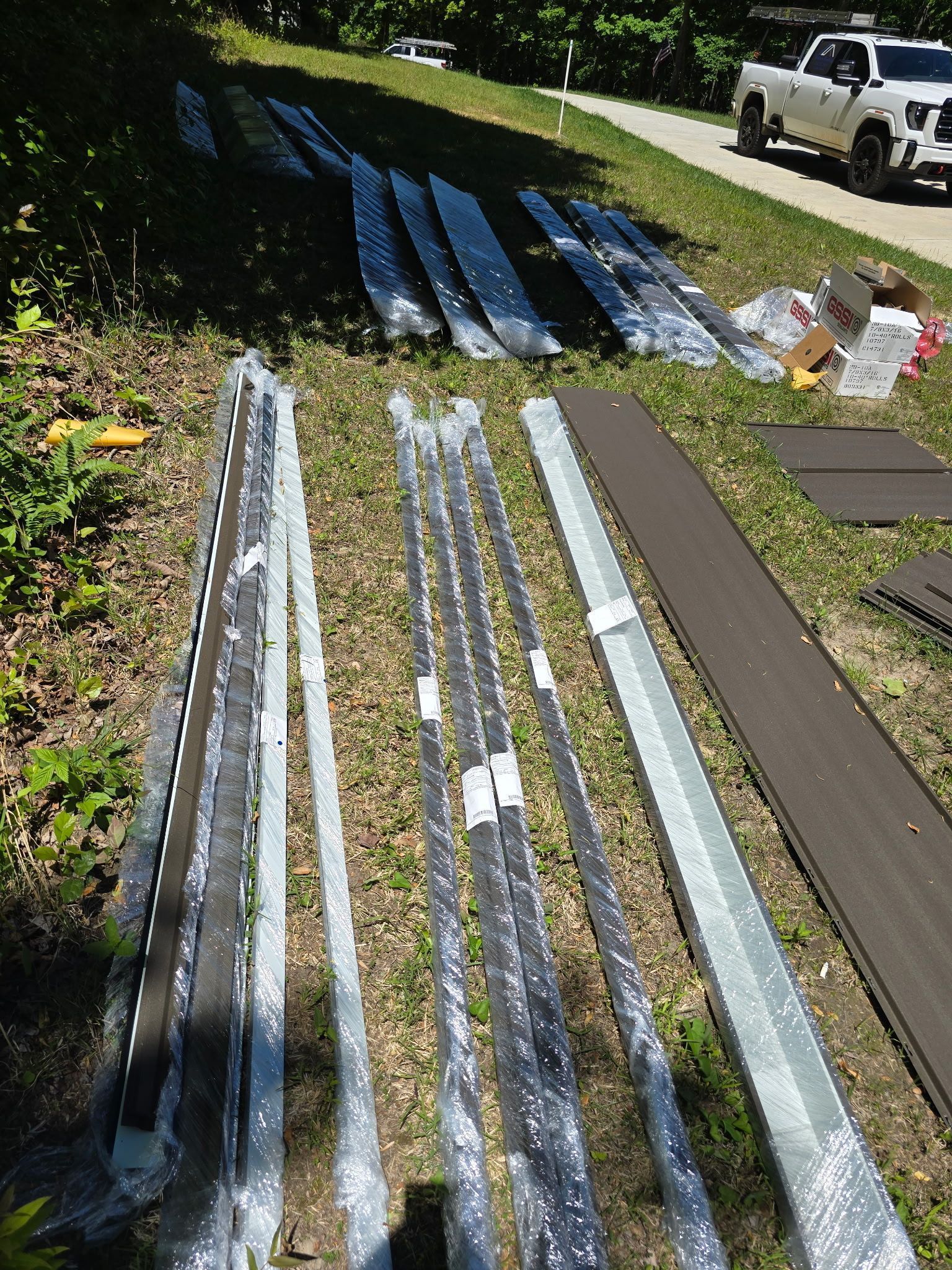 Metal roofing panels laid out on grass beside a white pickup truck in a sunny yard