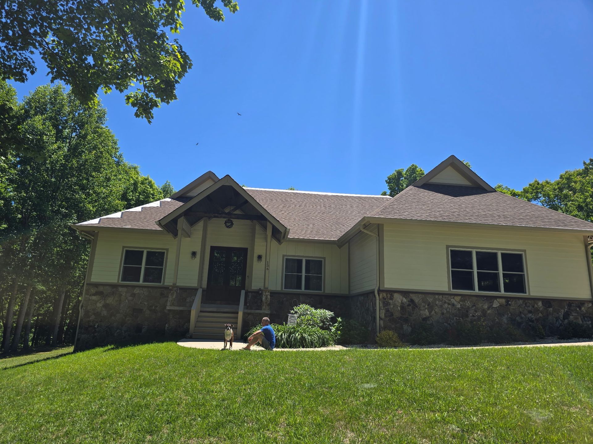 Single-story house with stone facade and green lawn under a blue sky