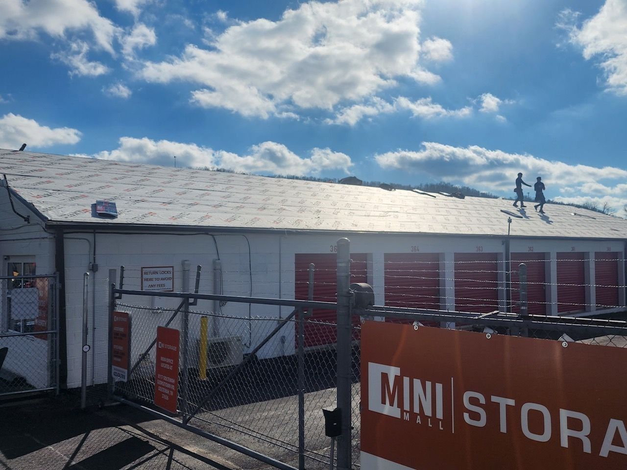 Buildings with red doors and trucks on a cracked asphalt lot under a cloudy sky.