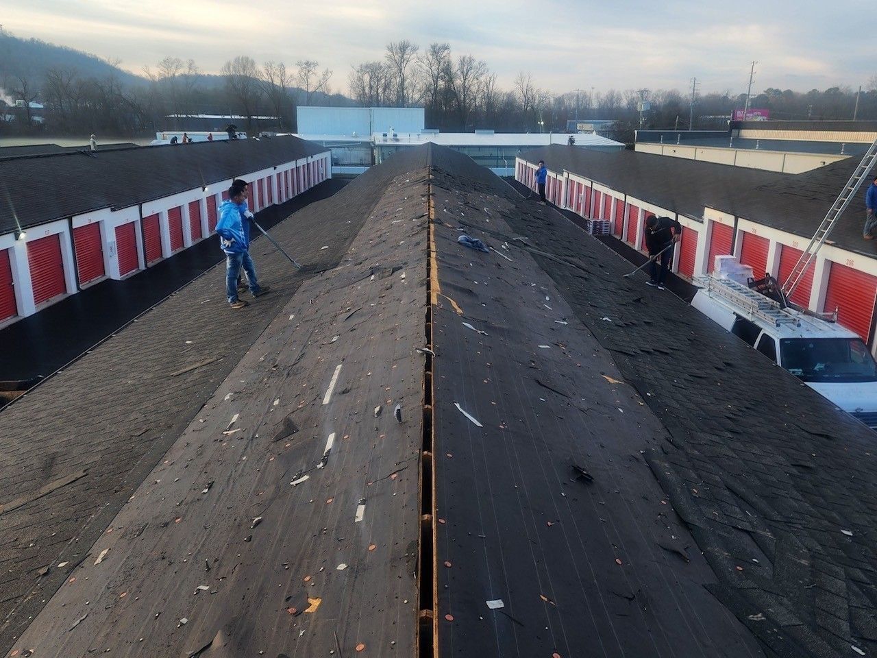 View of a white flat roof with equipment, under a sunset sky with a treeline and houses in the distance.