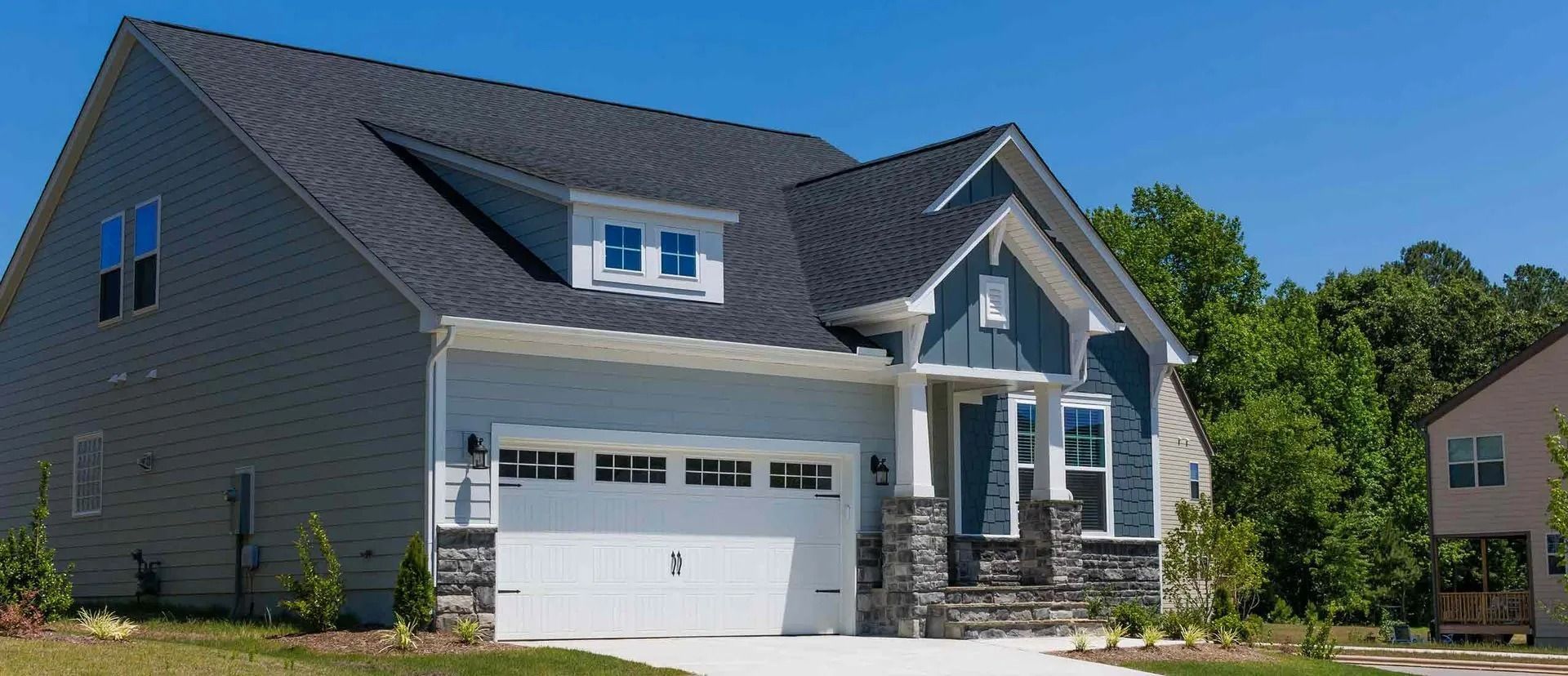 A two-story house with light blue siding, a dark gray roof, and a white garage door under a blue sky.