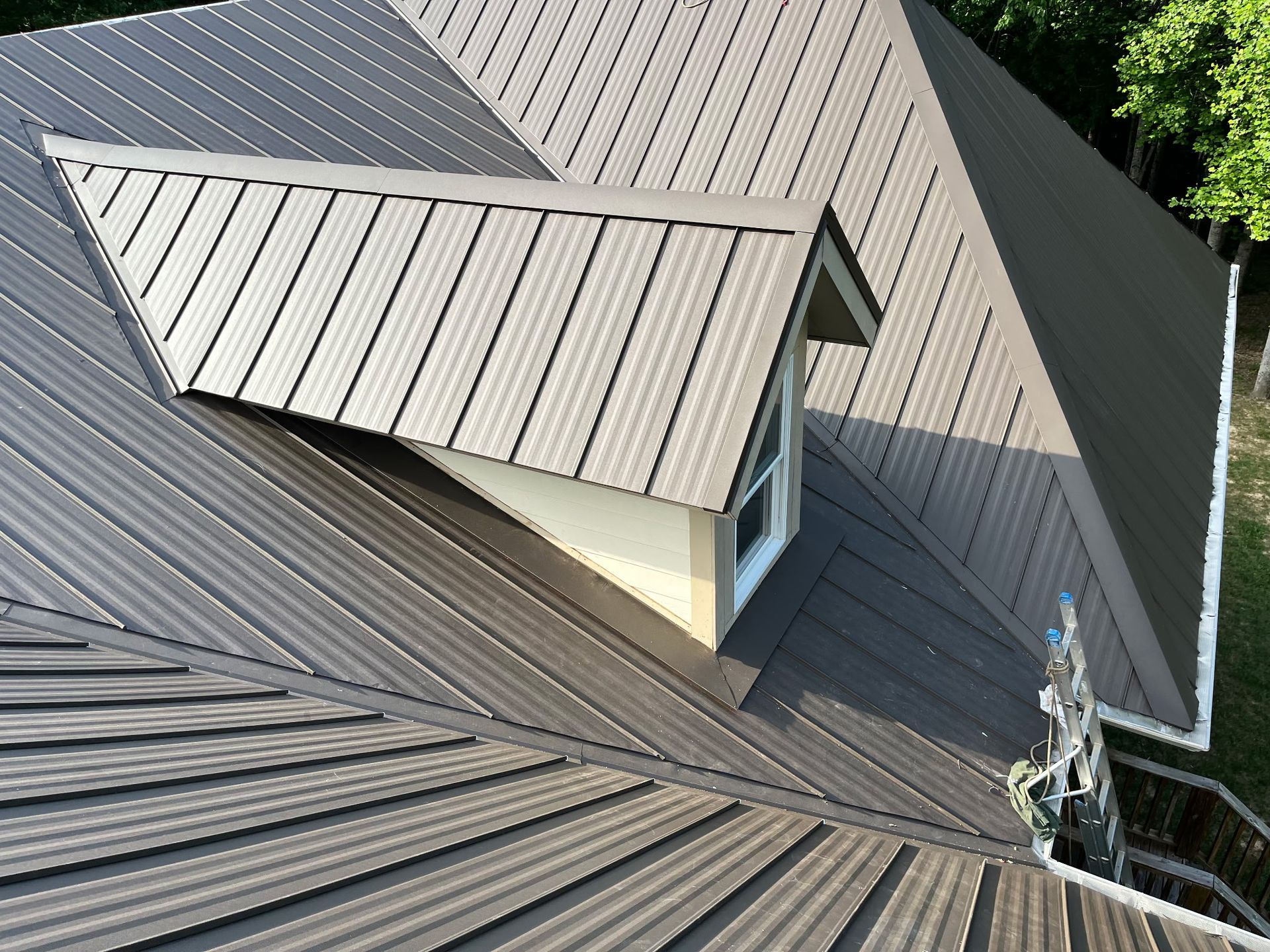 Roof with gray metal shingles and a beige dormer window on a house exterior.