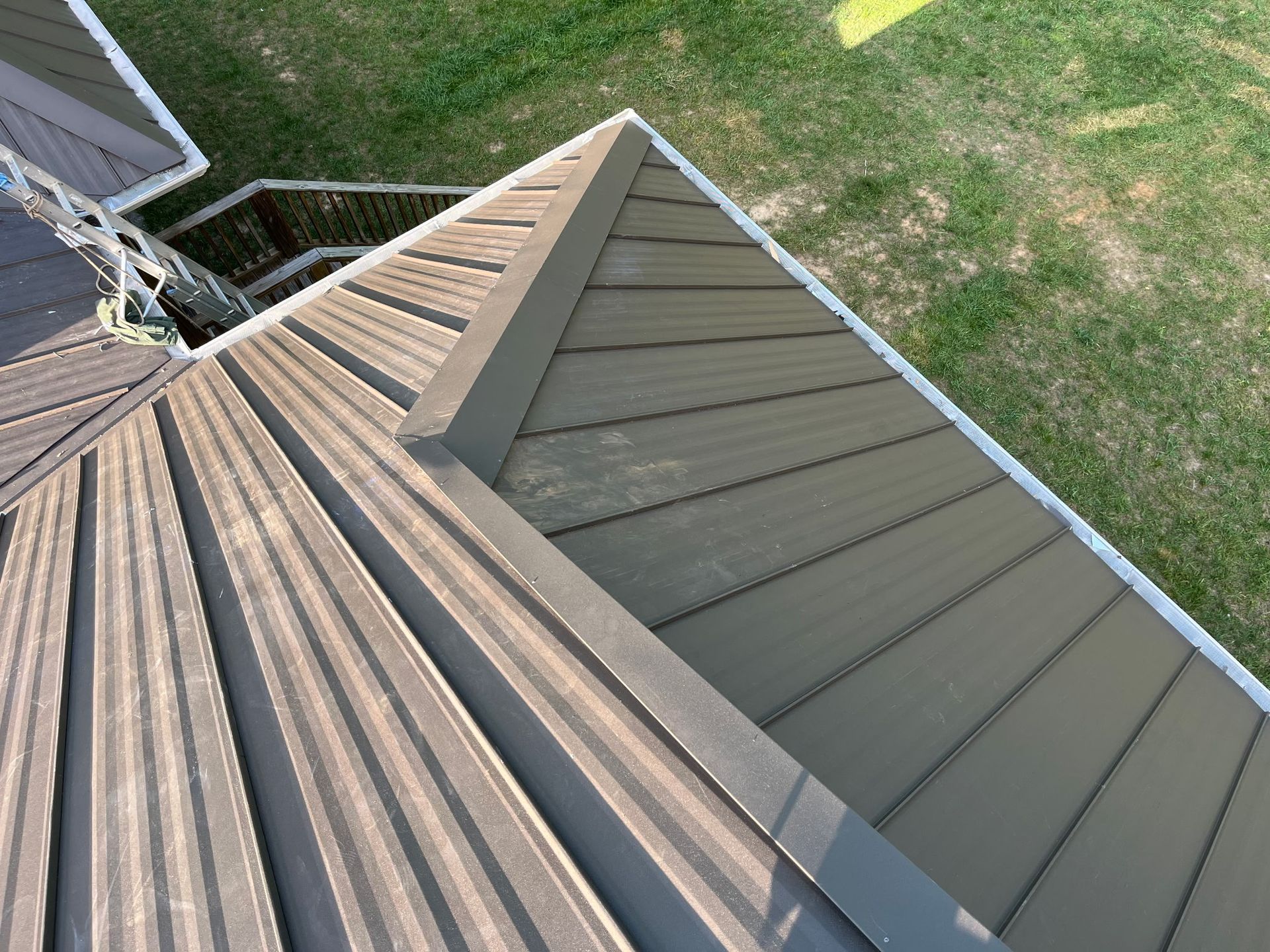 Aerial view of a house roof with gray metal panels and a grassy yard below