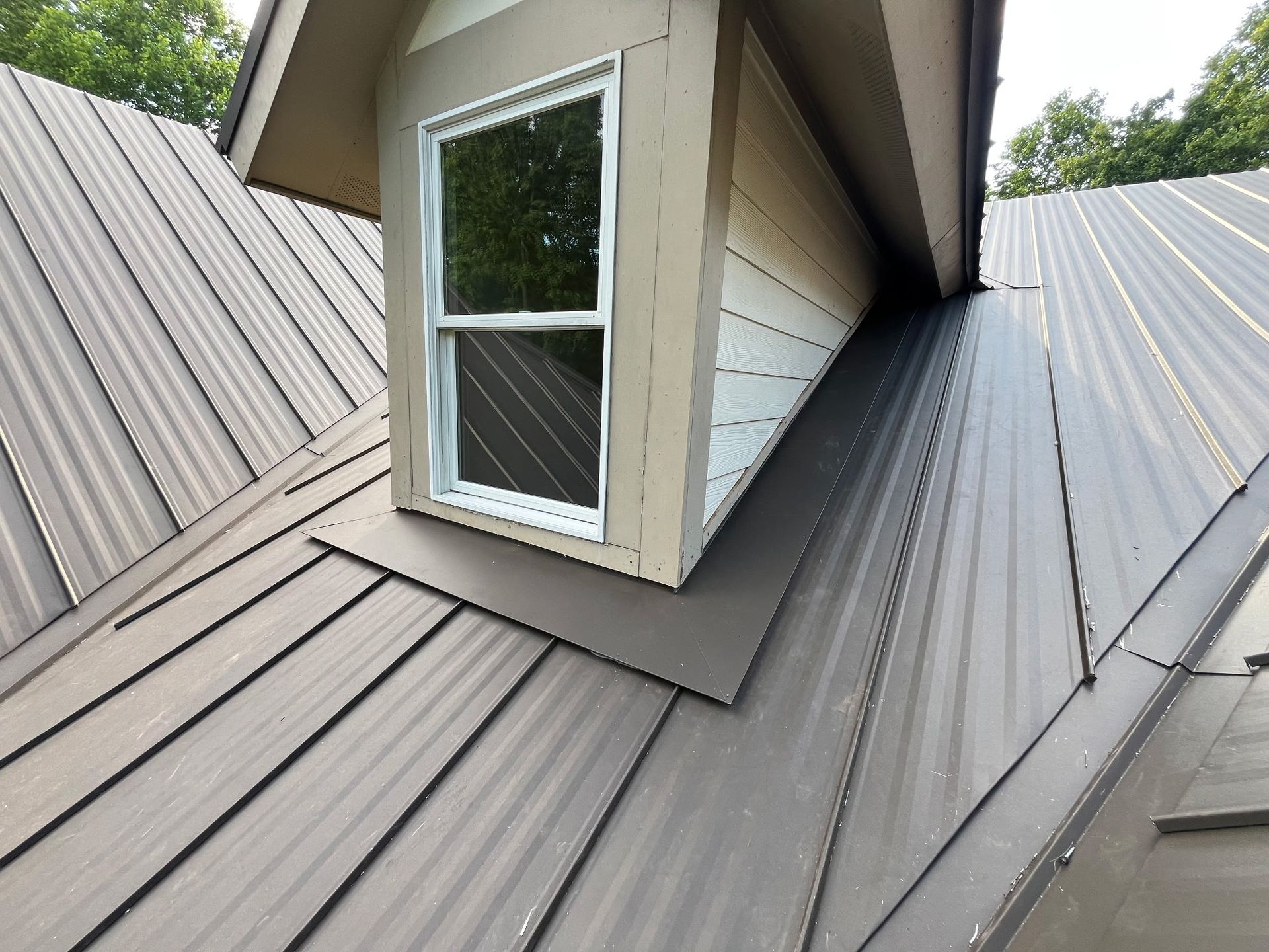 Dormer window with white trim on a gray metal roof, viewed from above