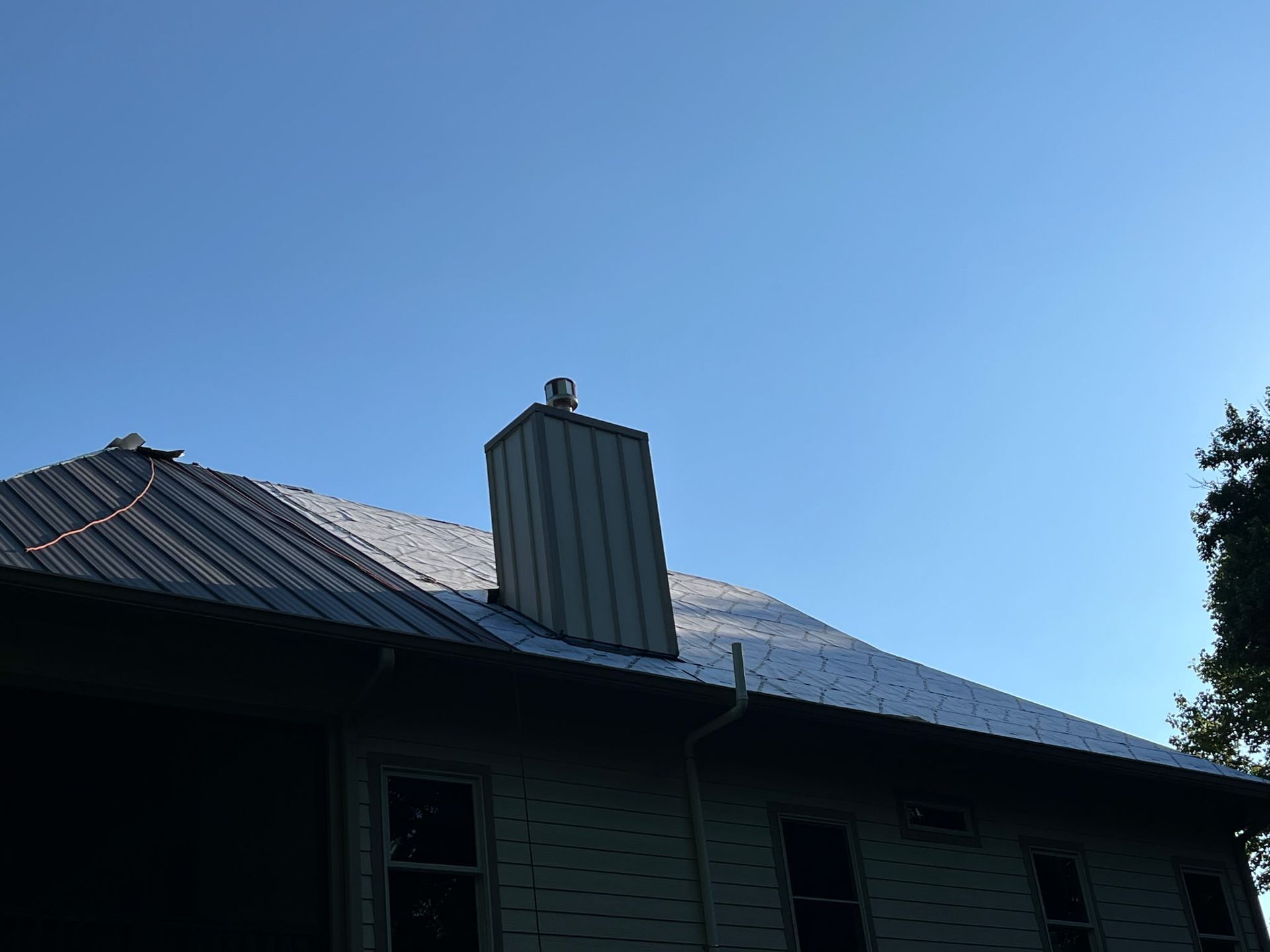 Dark house roof with a central chimney against a clear blue sky