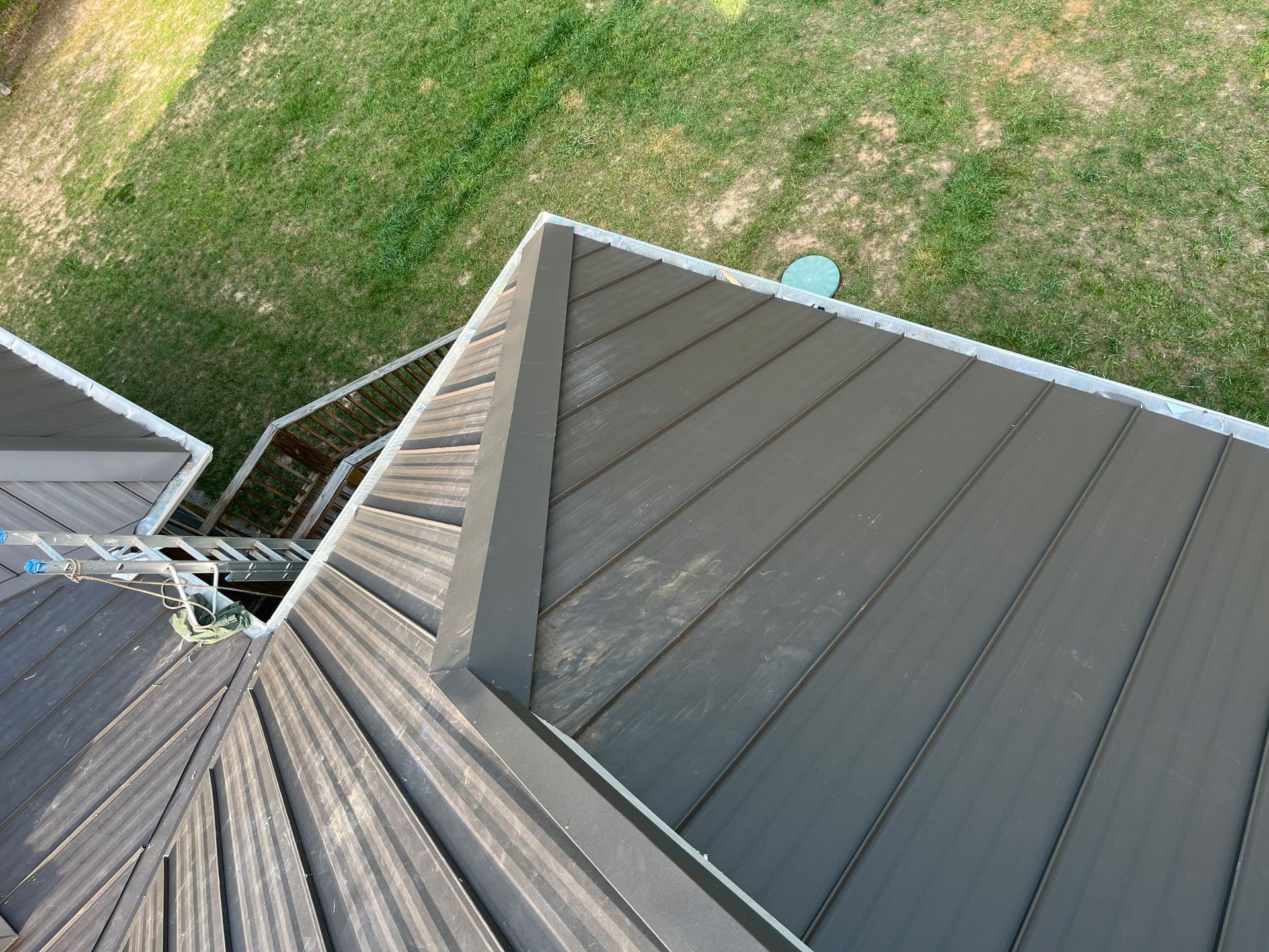 View from a roof peak showing gray metal roofing beside a grassy yard below.