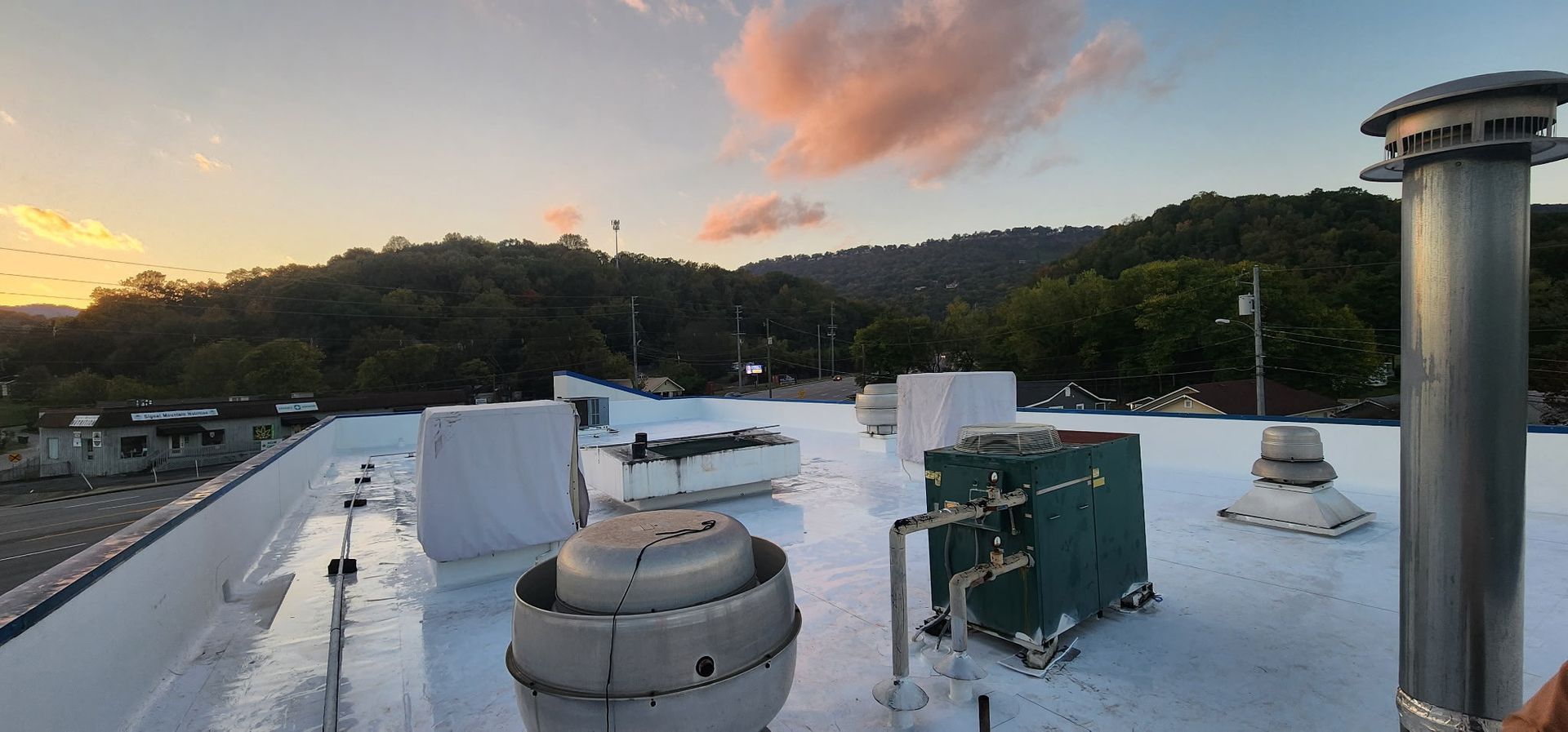 Rooftop view with equipment, mountain backdrop at sunset with pink and orange clouds.