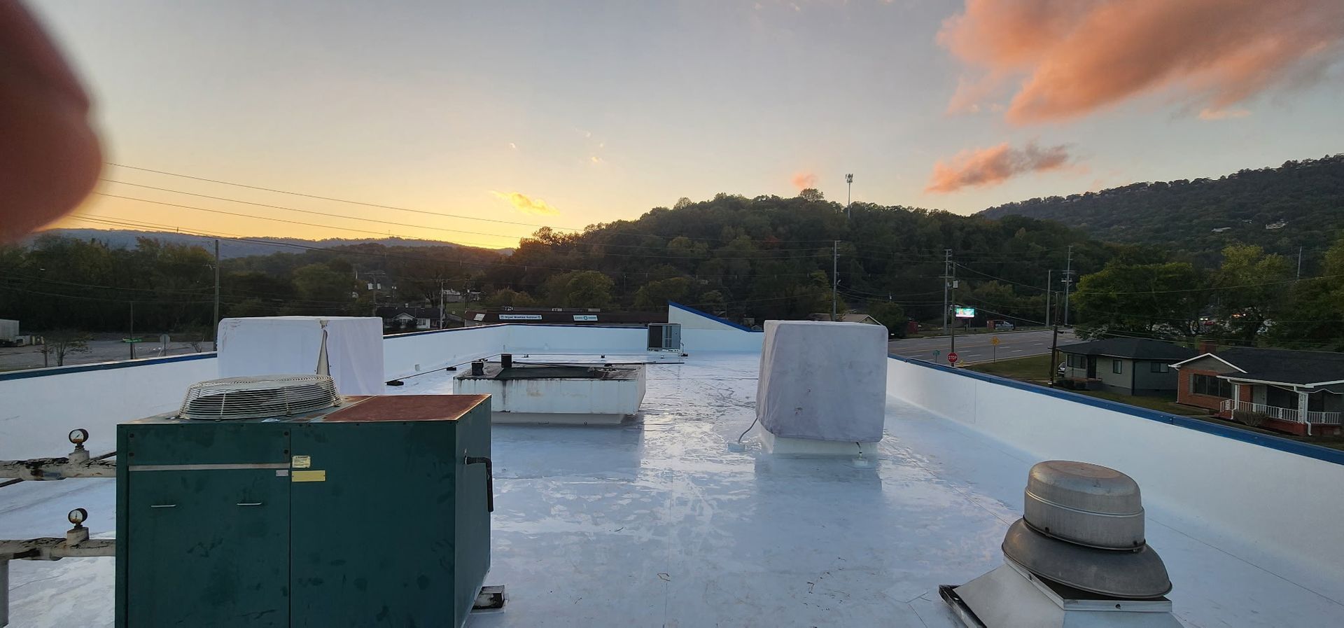 View from a roof at sunset; dark green hills in the distance, blue-white roof, equipment on roof.