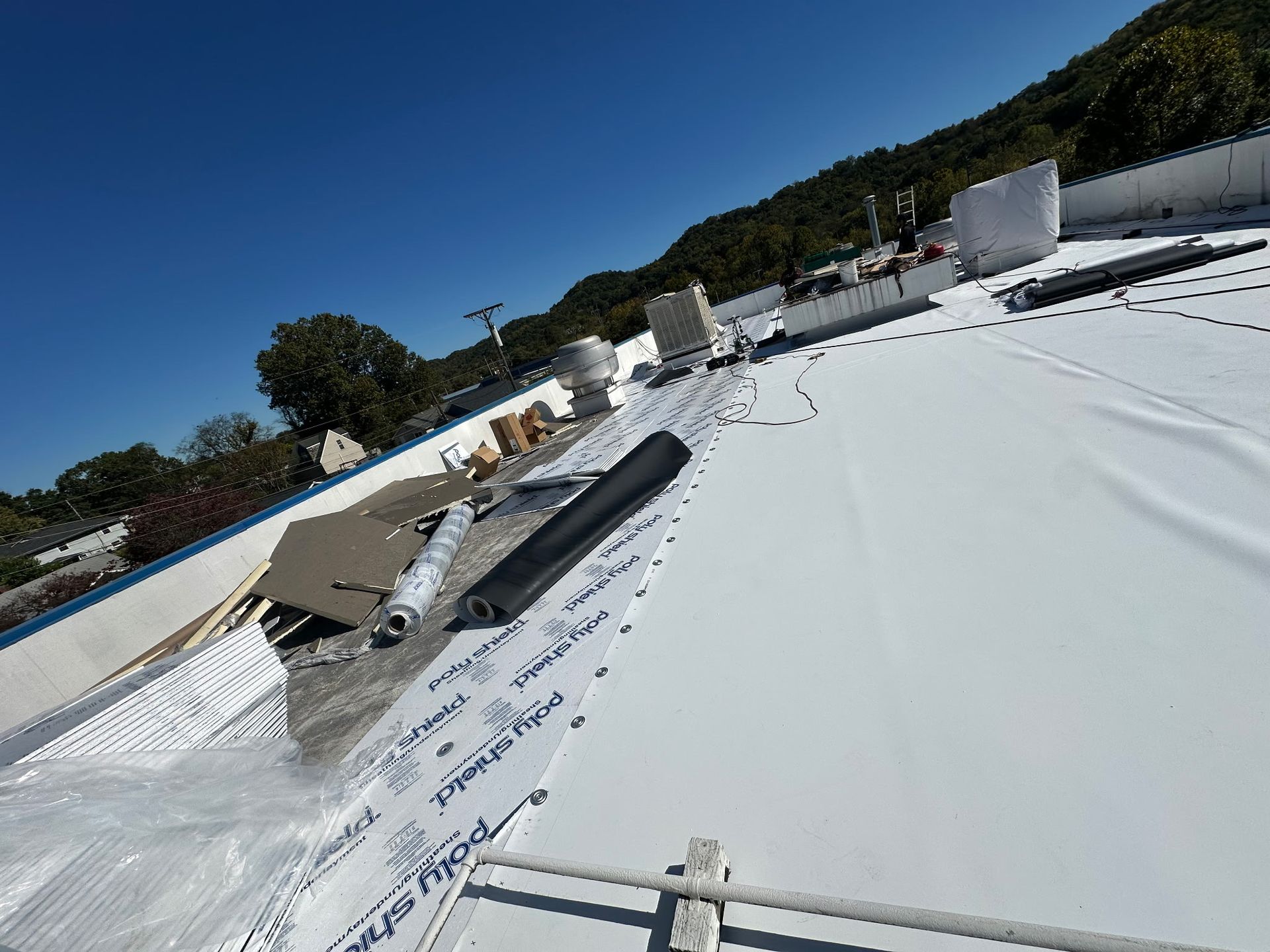 White commercial roof being installed with rolls of material and equipment on a sunny day.