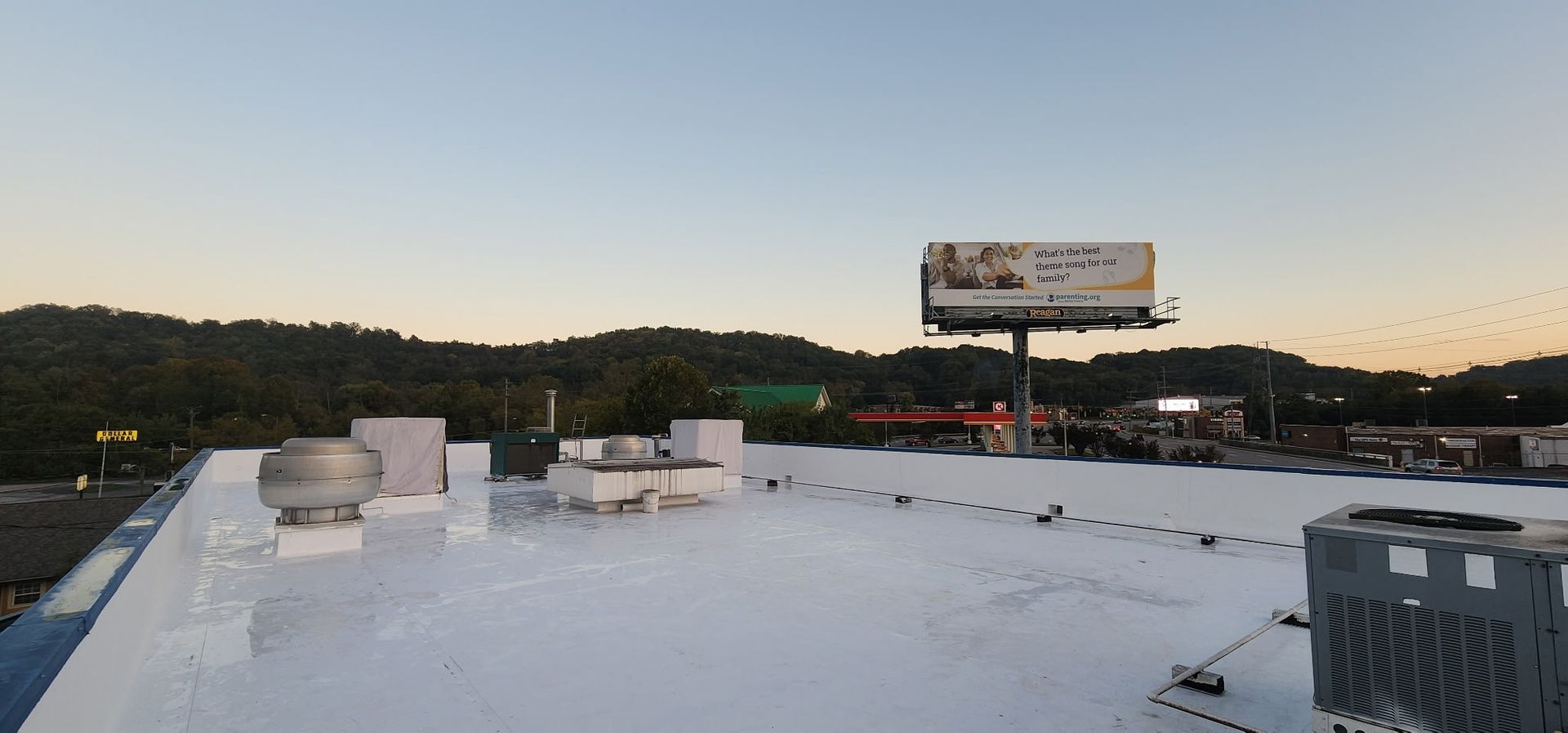 View from a white rooftop with a billboard in the distance. Overcast sky with trees in the background.