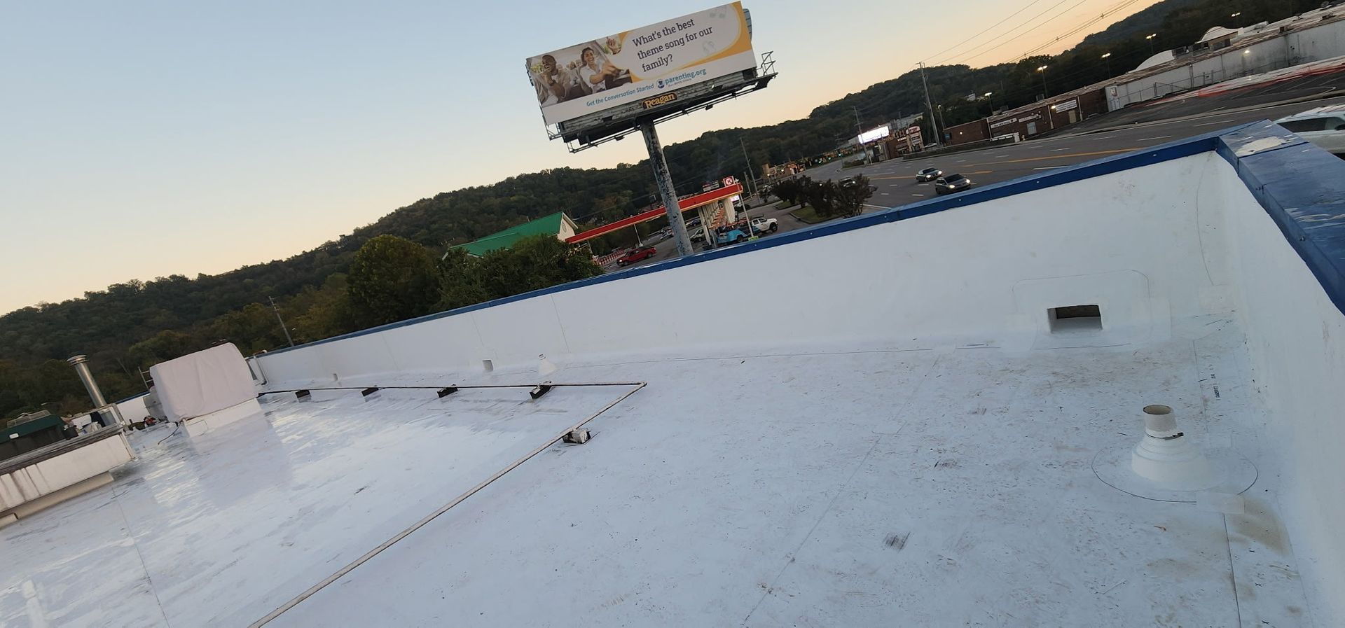 View from a white roof with a large billboard, trees, and road in the background. Blue and white trim.