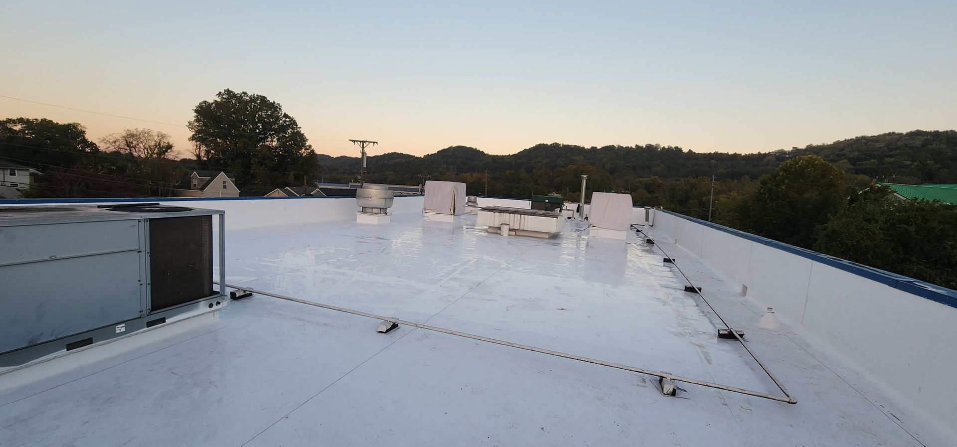 View from a commercial rooftop with vents and surrounding trees under a dusky sky.