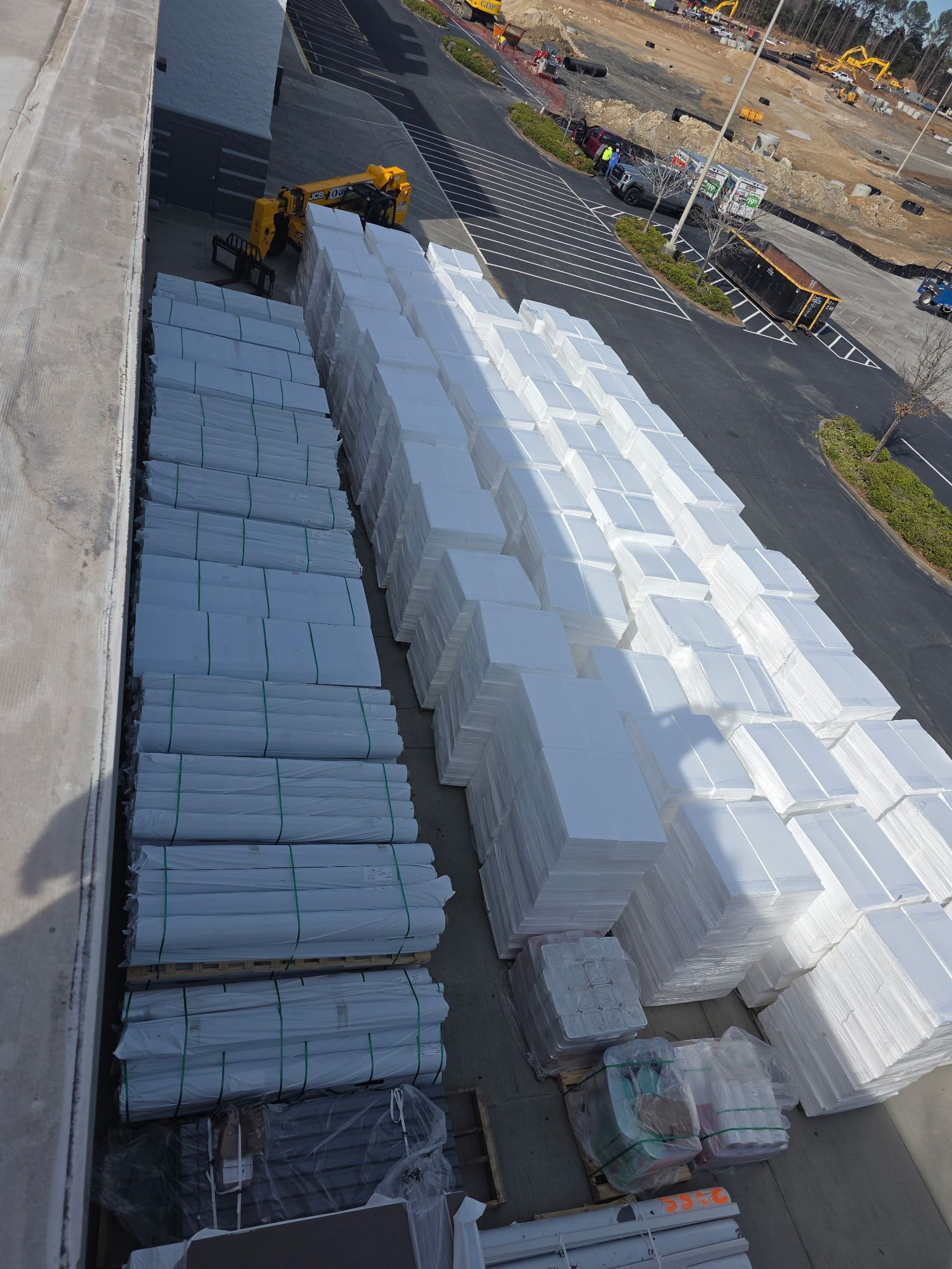 A semi-truck carrying lumber on a flatbed trailer, parked near a fence on a sunny day.