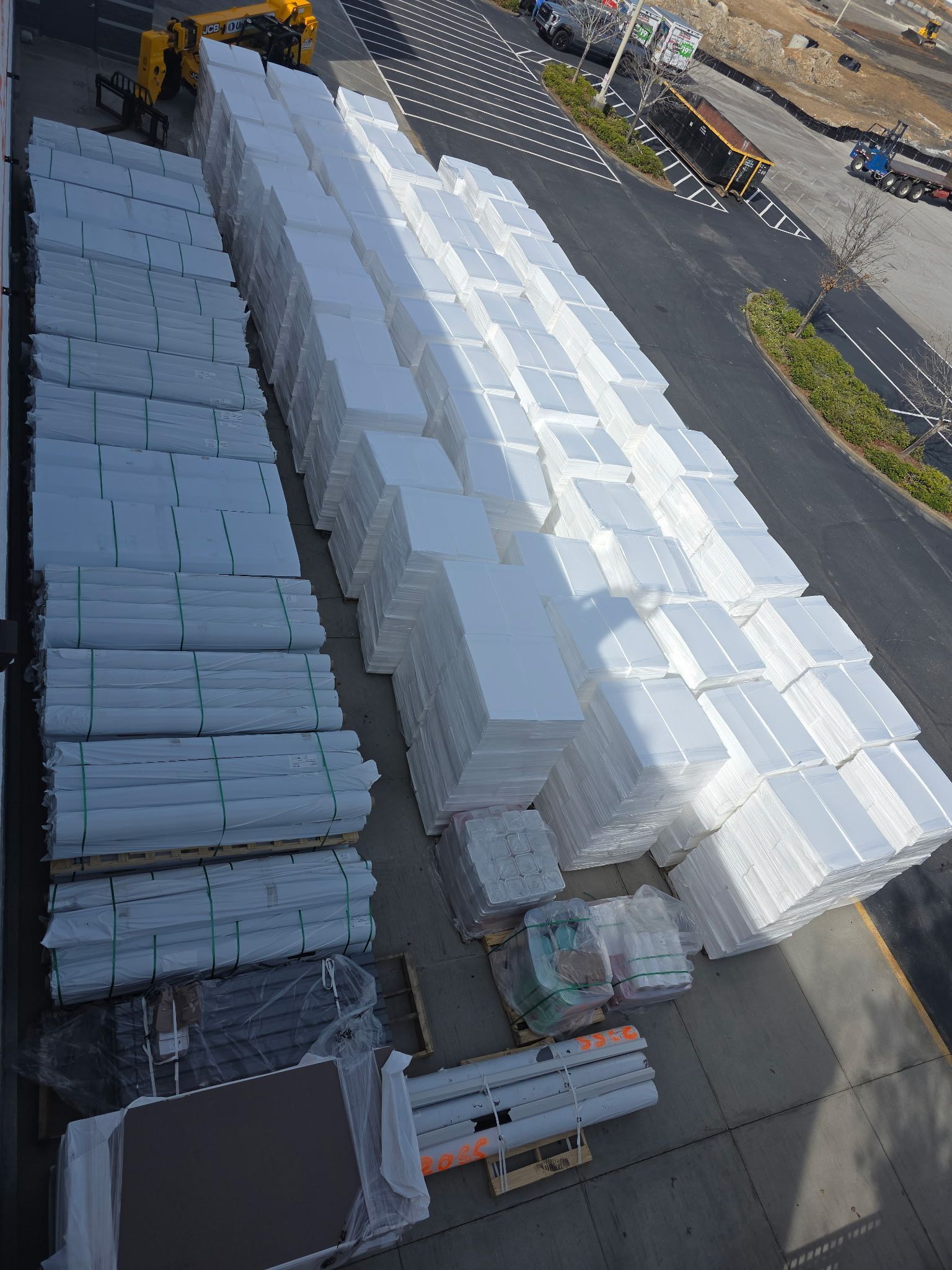 A flatbed truck transporting yellow construction equipment: a telehandler and a scissor lift, under a blue sky.