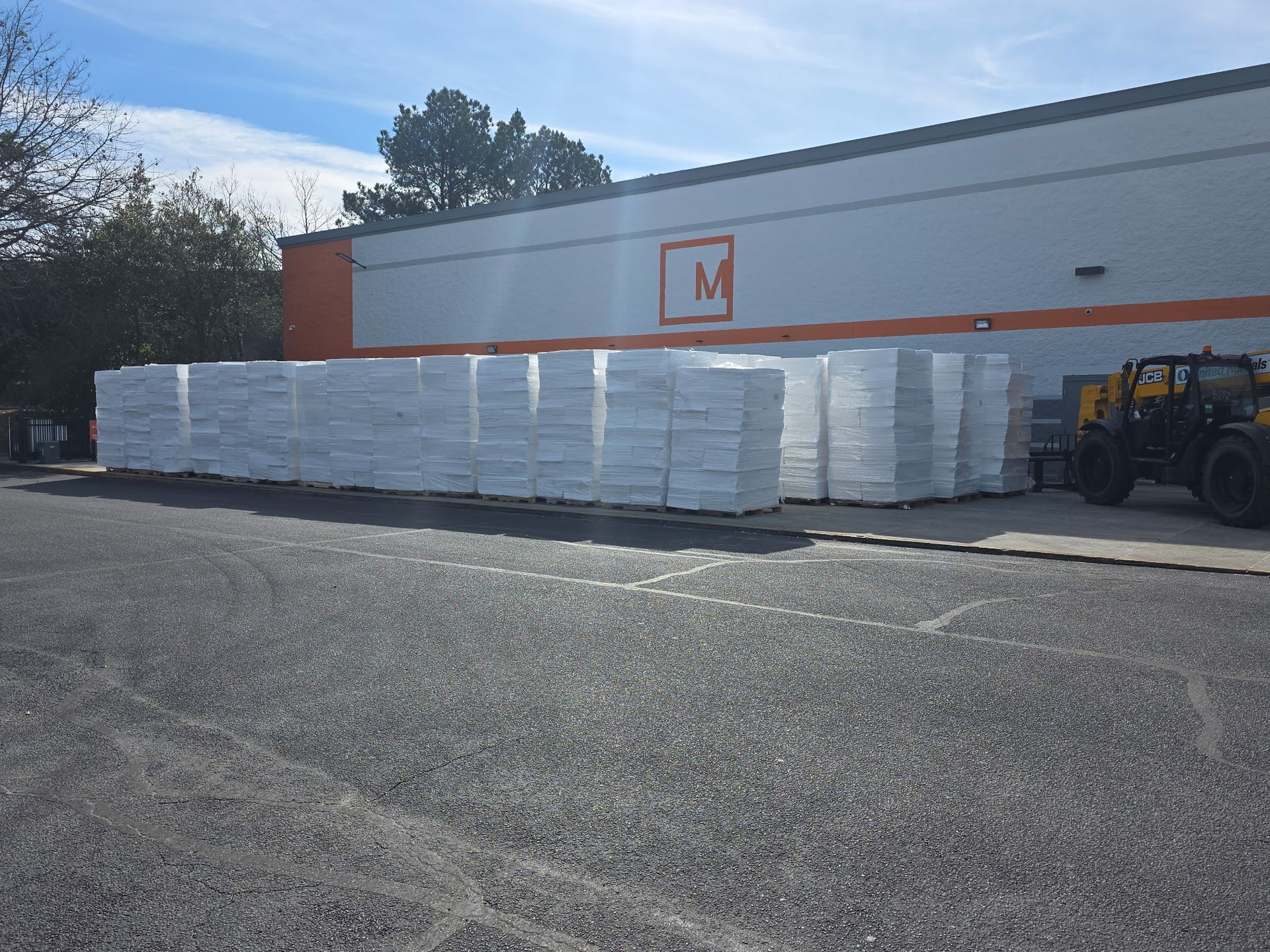Forklift loading pallets of white poles onto a flatbed trailer in a parking lot. Blue forklift.