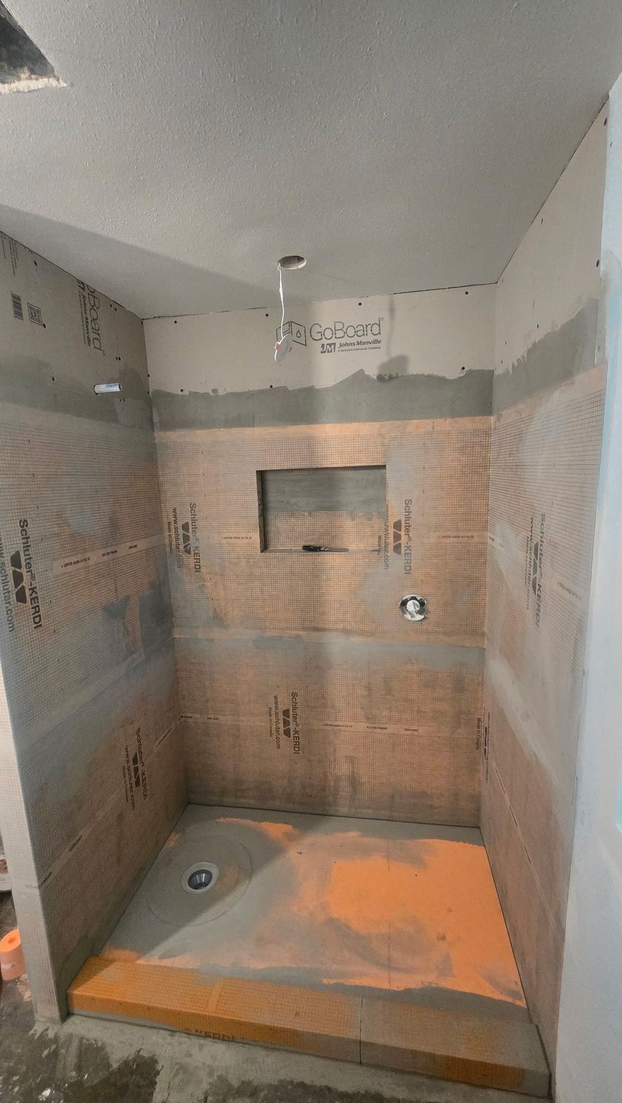 Shower under construction with orange waterproof membrane on walls and floor.