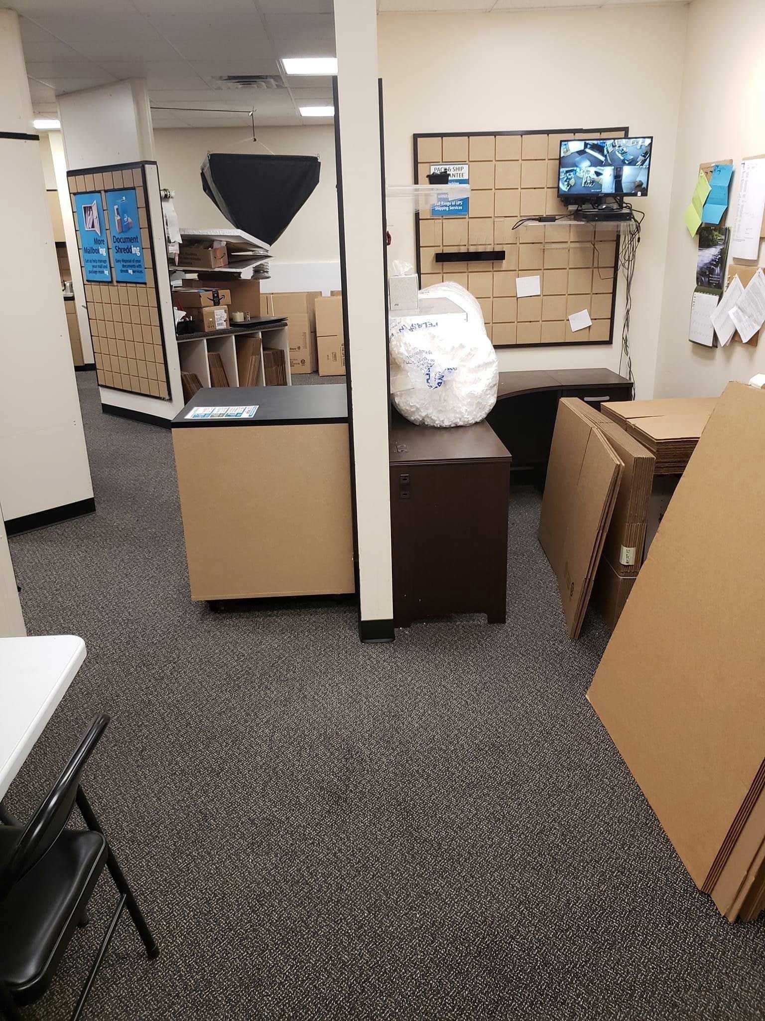 A cluttered office with cardboard boxes, dark furniture, and a rug.