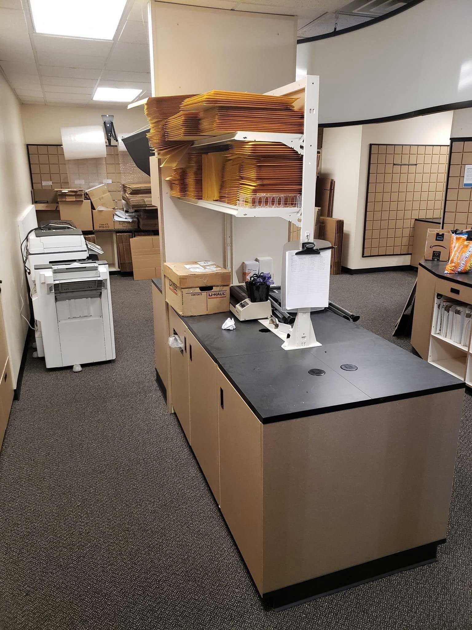 Office with printing equipment and mailing supplies on shelves and counter.