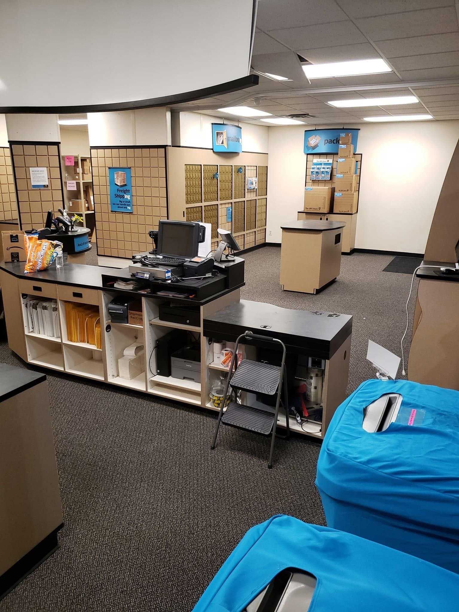 Interior of a shipping store, counter with computers, cardboard boxes, and blue bags.