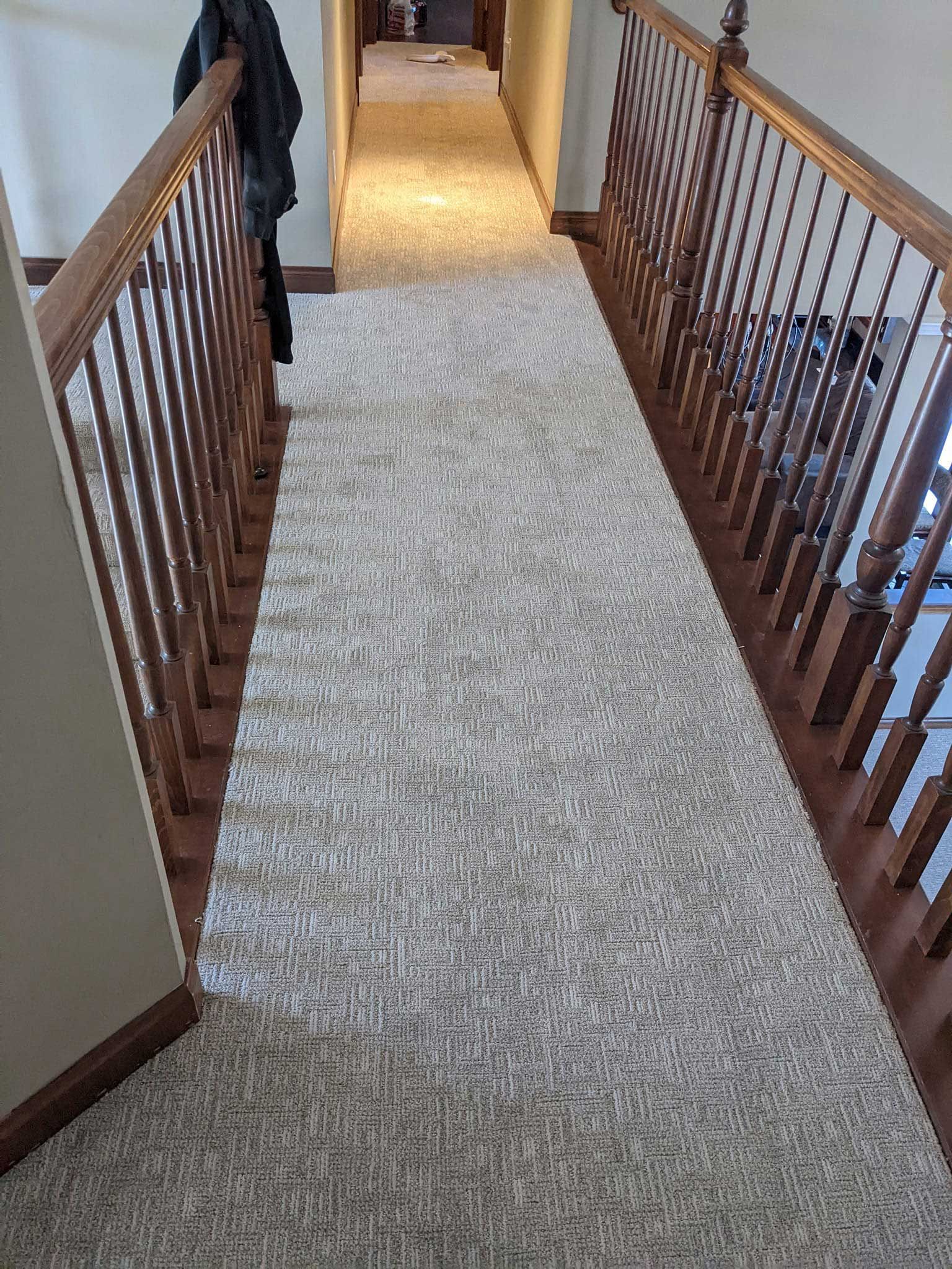 Hallway with beige carpet, wooden banisters, and a coat rack on the left.