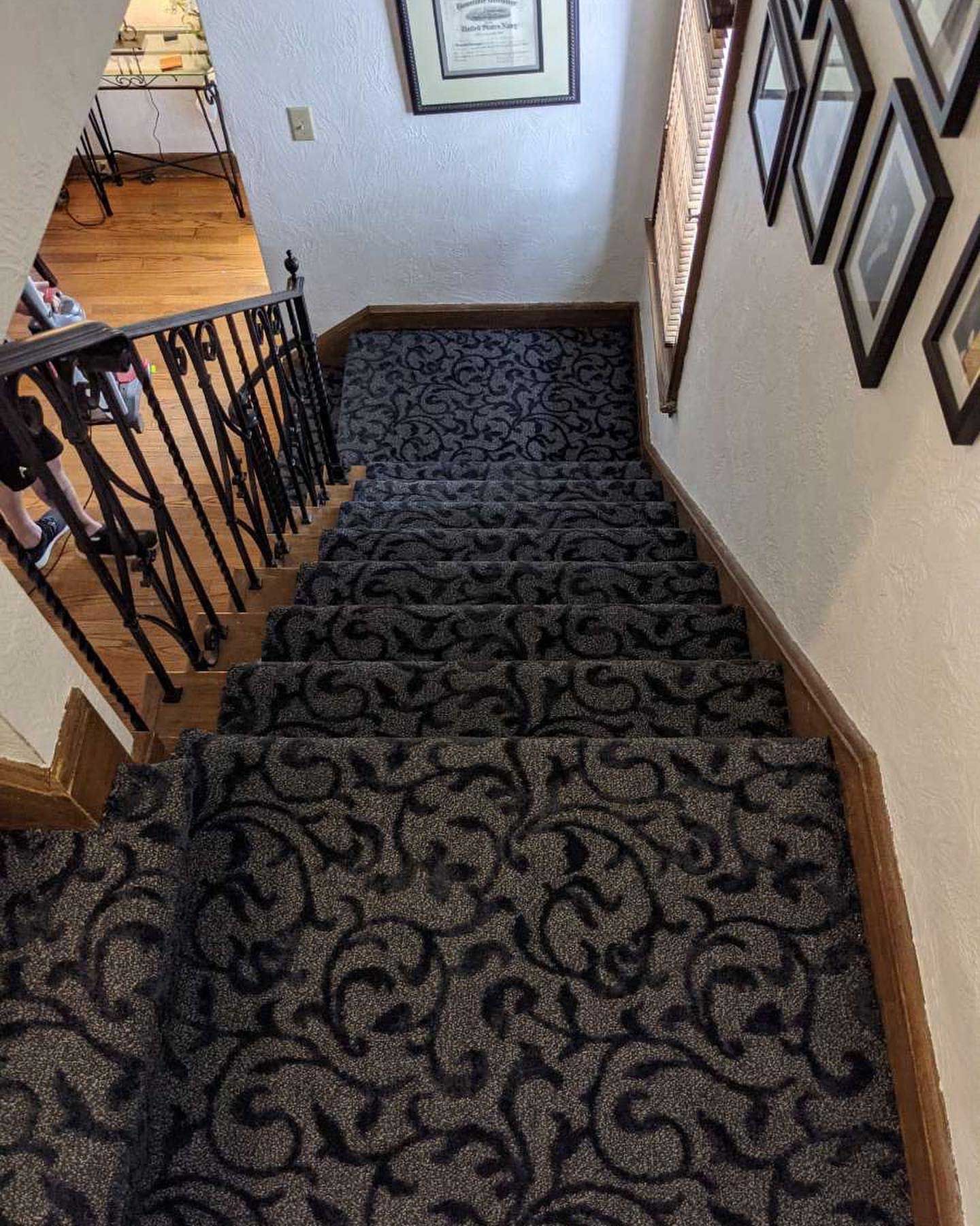 Staircase with patterned gray carpet and dark wooden railing and trim. Black and white framed pictures on the wall.