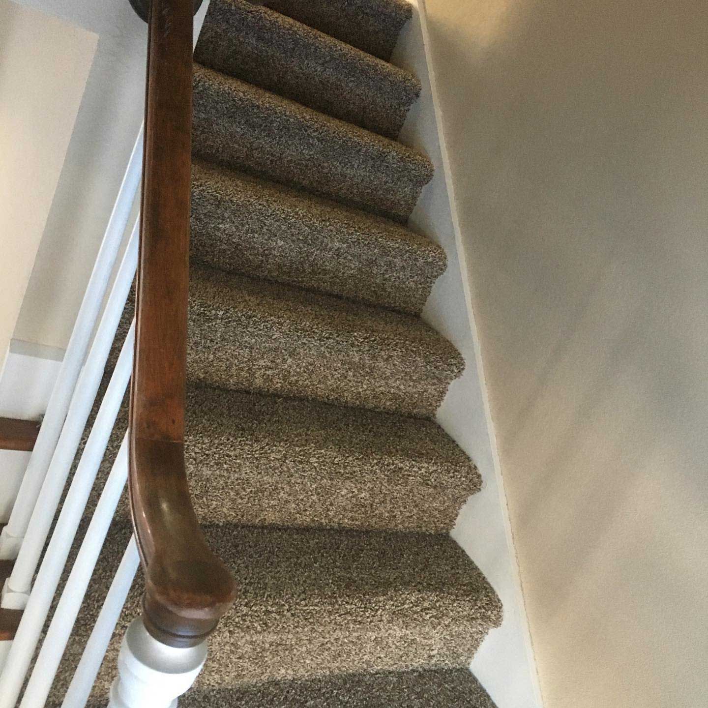Staircase with brown carpet and wooden handrail against a white wall.