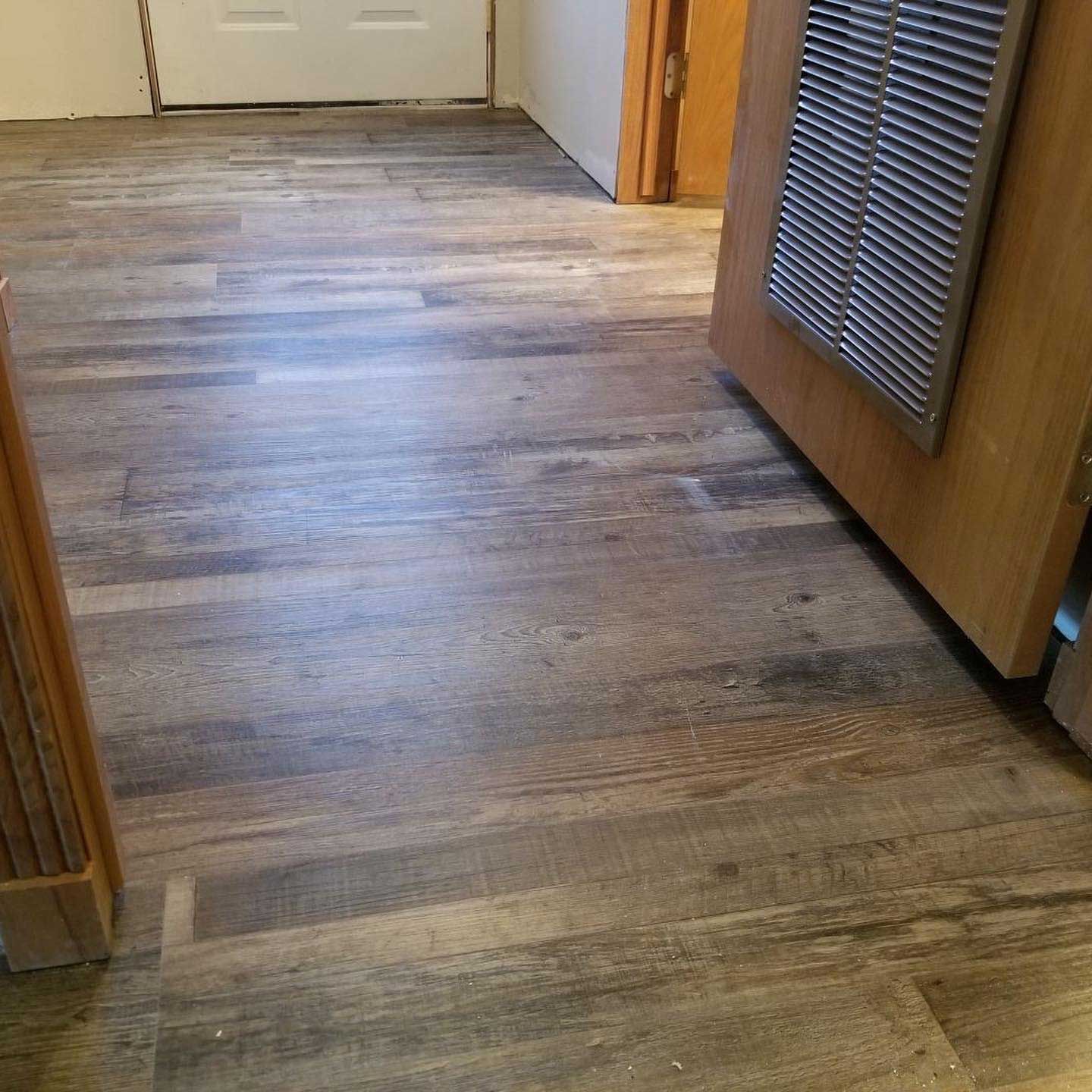 Wooden floorboards in a room with a light door and wooden cabinets.