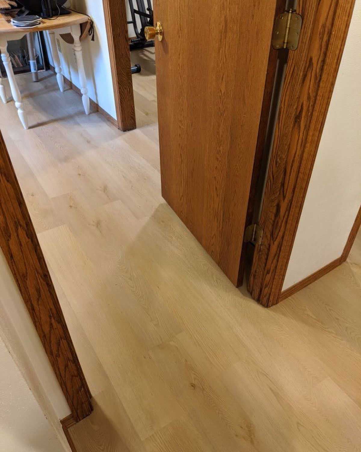 Light wood-look flooring with a partially open wooden door and a glimpse of a table in the background.