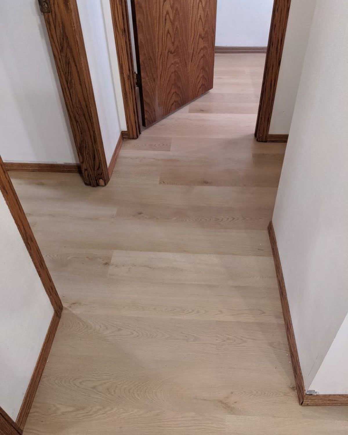 Hallway with light wood flooring, white walls, and brown door frames. A wooden door is slightly open.