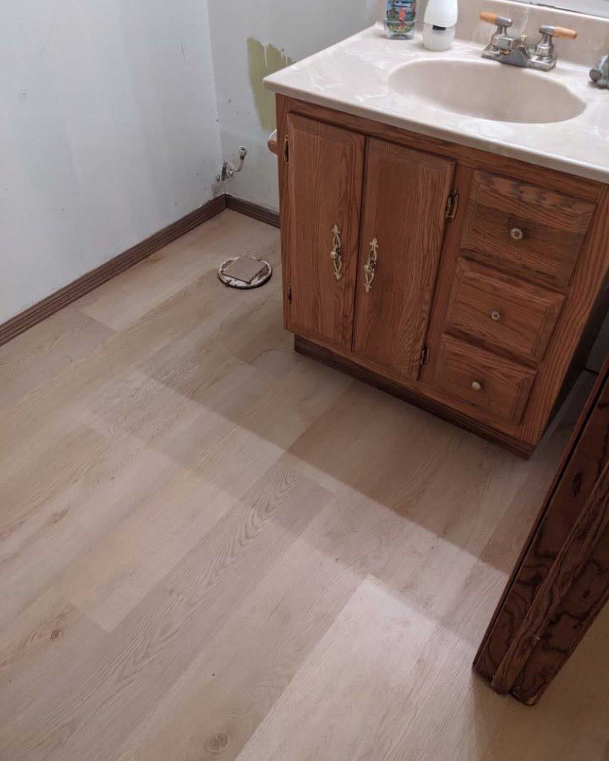 Bathroom with a wooden vanity, light-colored flooring, and a toilet flange.
