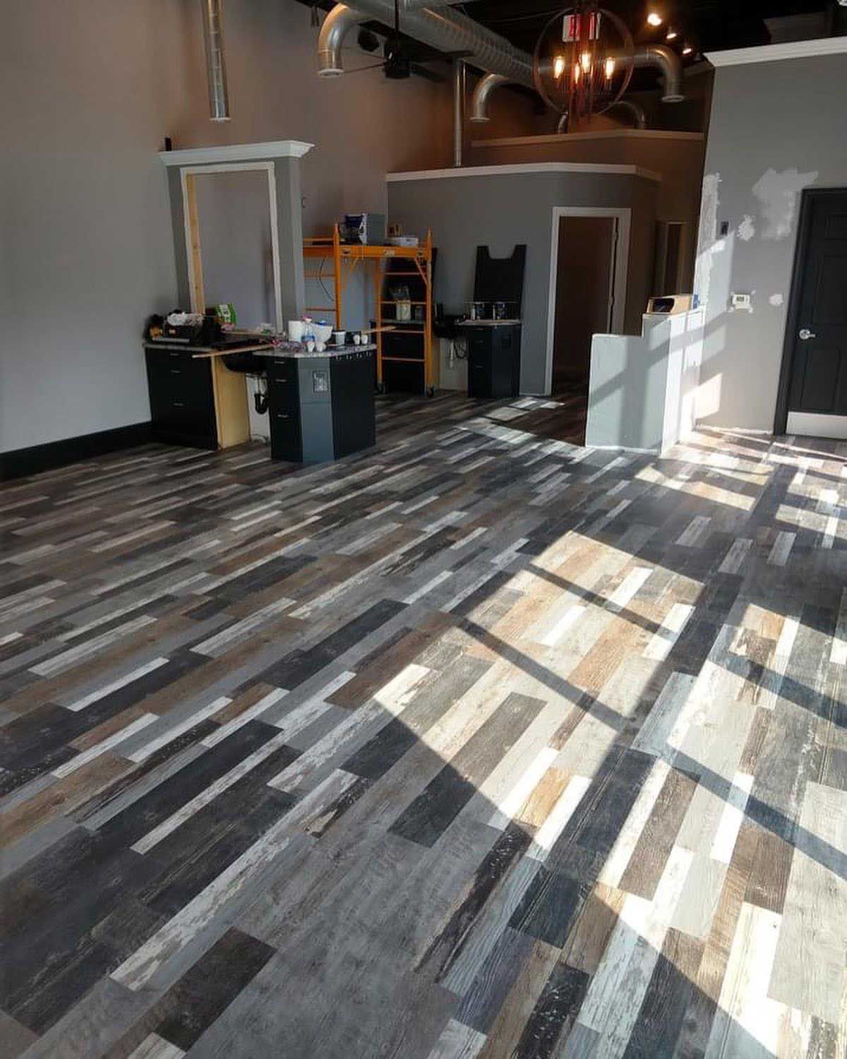Empty commercial space with wood-look flooring, desks, and shelving; sunlight streams in.