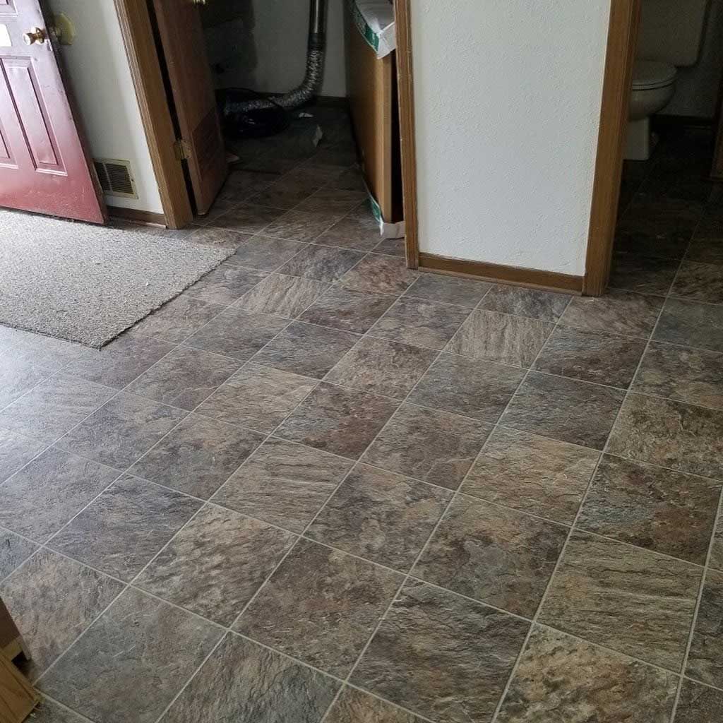 Brown and gray tile floor in a room with a red door and a white appliance visible in the background.
